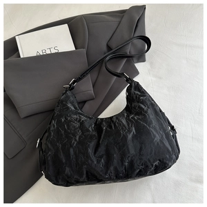 Detail of black crinkled texture hobo bag with adjustable strap on minimalist background
