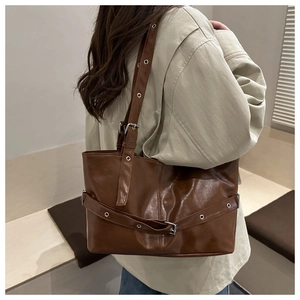 Detail view of large brown tote bag featuring industrial metal eyelets and adjustable straps
