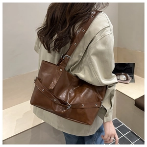 Detail of dark brown leather tote bag featuring stylish metal grommets and shoulder strap
