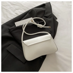 Detail of white leather shoulder bag with decorative knotted strap and gold metal tips