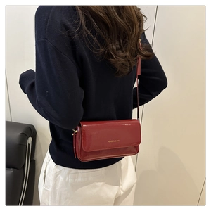 Close-up of a glossy red patent leather crossbody bag with gold logo on a model