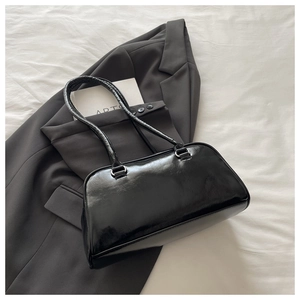 Minimalist black glossy leather shoulder bag displayed on a stylish grey suit jacket