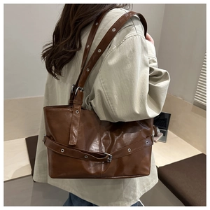 Detail of a deep brown PU leather tote bag with silver metal eyelets and adjustable straps