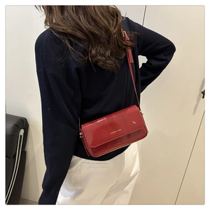 Detail of a shiny red patent leather crossbody bag with gold logo on a fashion model