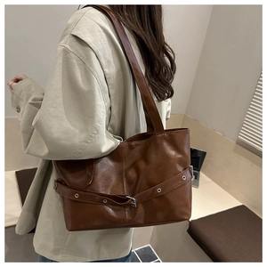 Detailed side view of a large brown leather tote bag worn by a model in a minimal setting
