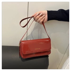 Detail of red patent leather crossbody bag with metallic logo and sleek flap closure