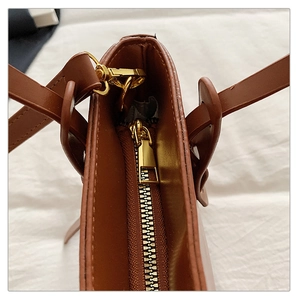 Détail de la fermeture éclair dorée et des crochets métalliques sur un sac seau en cuir marron