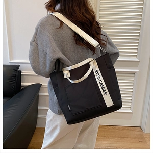 Detail of black nylon tote bag with white branded straps and large front pocket