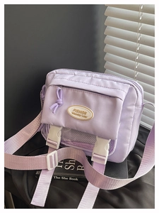 Detail of lavender nylon crossbody bag featuring dual ivory buckles and logo plate