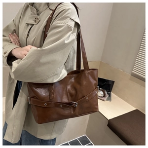 Detail of dark brown leather tote bag showing decorative belt with silver metal eyelets