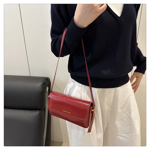Detail of red patent leather baguette bag with gloss finish and gold logo on the shoulder