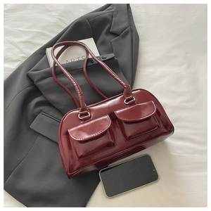 Detail of dark red glossy leather shoulder bag featuring two front pockets on a gray blazer