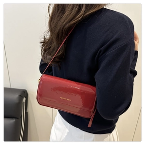 Detail of red patent leather square shoulder bag with gold logo and sleek mirror finish