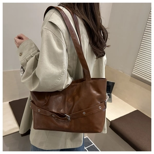 Detail of dark brown tote bag featuring decorative leather straps and metal eyelets