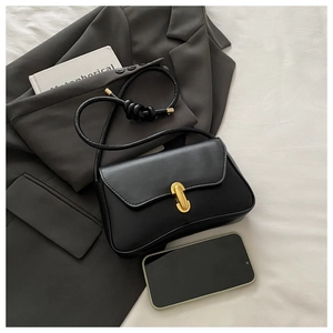Detail of black matte leather shoulder bag with gold metal buckle and knotted rope strap