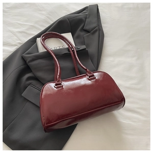 Detail view of burgundy glossy leather handbag with silver buckles and slim handles