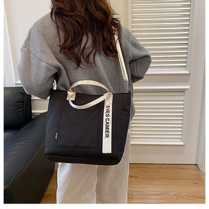Detail of black canvas tote bag showing white handles and adjustable shoulder strap