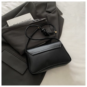 Detail of black matte shoulder bag featuring unique knotted strap and sleek flap closure