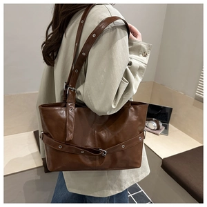 Detail of dark brown tote bag featuring interwoven straps and silver metal buckles