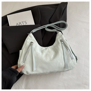 Detail of mint green hobo tote with tassel zippers on a black blazer background