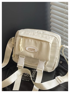 Detail of cream nylon crossbody bag featuring double buckles and adjustable shoulder strap
