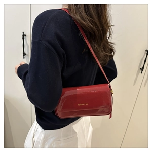 Red patent leather shoulder bag with gold lettering shown on person against blue sweater