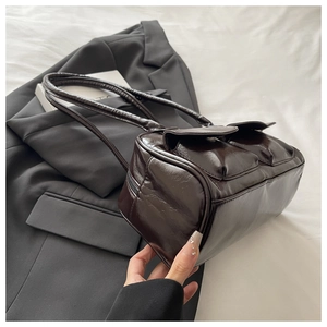 Detail of dark brown polished leather shoulder bag with pockets on grey suit background