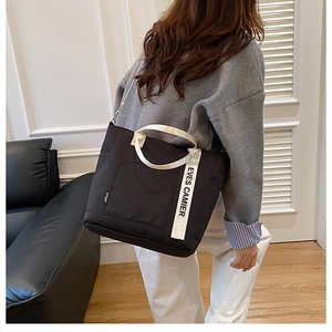 Detail of a black canvas lunch tote with white 'EVES CAMIER' straps for daily commuting