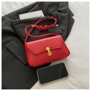 Detail of red leather shoulder bag with gold U-shaped metal clasp and knotted strap