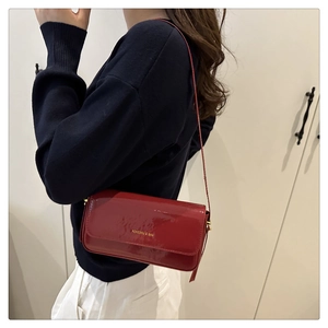 Detail of elegant dark red patent leather shoulder bag with a polished gold finish logo