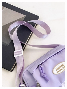 Close-up of light purple nylon crossbody bag with logo patch and adjustable strap