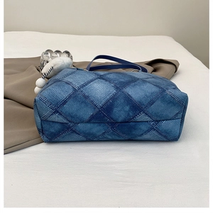 Detail of blue denim tote bag with quilted diamond pattern and white pom-pom charm
