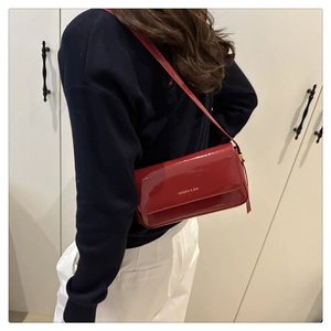 Detailed view of red patent leather shoulder bag with gold logo on a fashion model