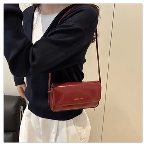 Detail of red patent leather crossbody bag with gold lettering shown on model