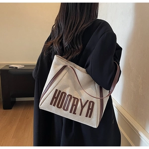 Detail of the HOORYA canvas tote bag with brown leather trim shown on shoulder