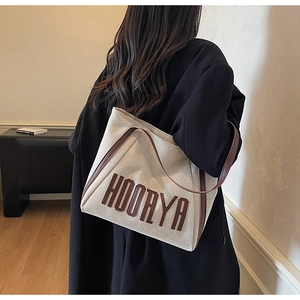Detail of off-white canvas tote with HOORYA lettering and brown leather handles