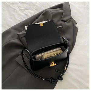 Detail of black leather handbag with gold twist lock on grey suit and white bedding