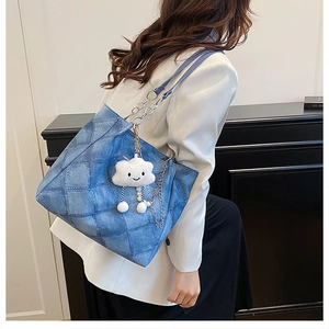 Detail of blue denim tote bag with quilted stitching, silver chain strap, and plush charm