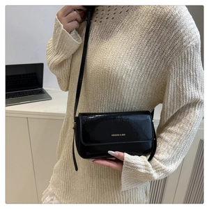 Close-up of black glossy patent leather shoulder bag with gold lettering and adjustable strap