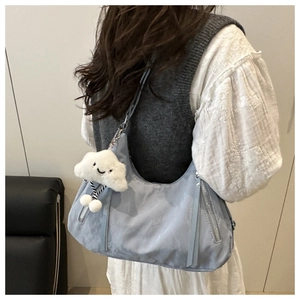 Close-up of light blue nylon crescent bag with plush cloud charm and silver zippers