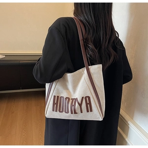 Detailed back view of a beige canvas tote bag with brown leather straps and text print