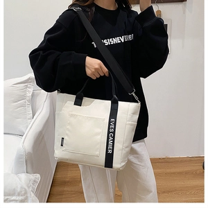 Detailed shot of white canvas tote bag with functional front pocket and wide strap