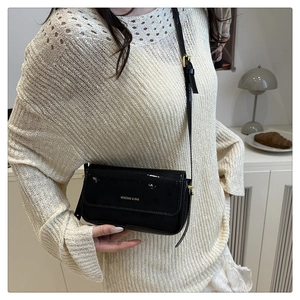 Close-up of black patent leather crossbody bag with golden logo on adjustable shoulder strap