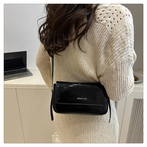 Detail of a black patent leather shoulder bag worn with a beige knit sweater