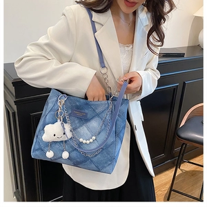 Detail of blue denim tote bag with quilted pattern, metal chains and pearl charms