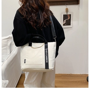Rear view of model wearing white nylon tote bag with black strap in a cozy home setting