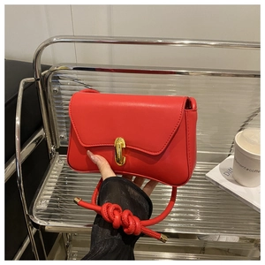 Red matte leather bag detail featuring a golden cylindrical lock and knotted shoulder strap