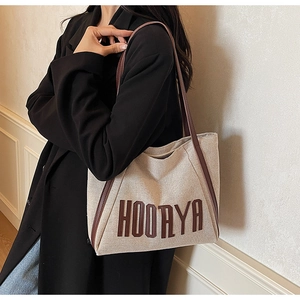 Detail of beige canvas tote with brown leather trim and HOORYA print on shoulder