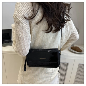 Detailed view of black patent leather crossbody bag worn by a model in a modern room