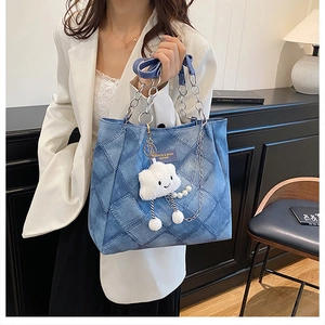Detail of blue denim tote bag with quilted pattern, silver chain, and plush cloud charm